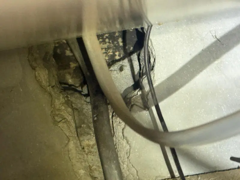 Inspection camera view of a mouse access hole where pipes pass through crumbling plaster